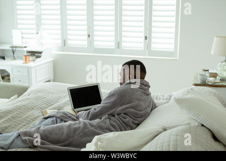 Mann mit Laptop im Bett im Schlafzimmer an komfortables Zuhause liegen Stockfoto
