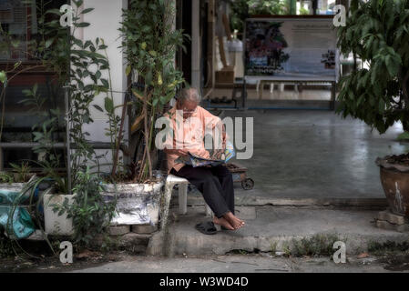 Man Zeitung lesen, auf dem Gehweg vor seinem Haus. Thailand Südostasien Stockfoto