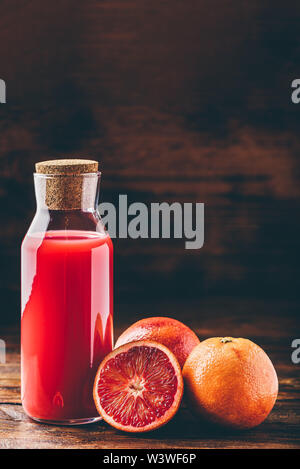 Flasche Blut Orangensaft mit halbierten Frucht auf hölzernen Tisch Stockfoto