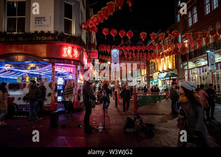 LONDON, ENGLAND, 10. Dezember 2018: Straßenmusiker spielt die Gitarre unter Neon Lichter in Chinatown, durch Chinesische Laternen während Weihnachten dekoriert Stockfoto