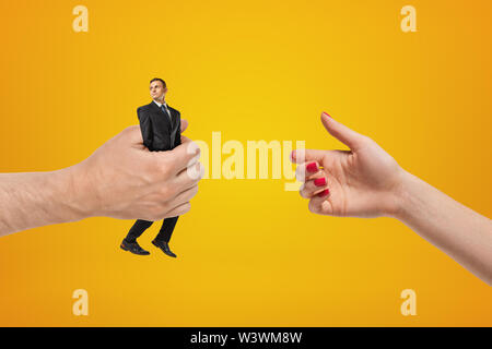 Die Hand auf der linken Seite halten kleine Geschäftsmann und geben ihm die Frau, deren Hand auf der rechten Seite auf gelben Hintergrund. Stockfoto