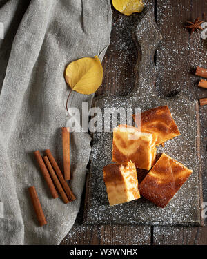 Quadratische Scheiben von Hüttenkäse und Pumpkin Pie auf einem Holzbrett, Dessert ist bestreut mit Puderzucker, Ansicht von oben Stockfoto