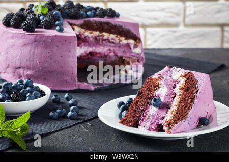 Festliche Kuchen, Heidelbeere und Blackberry Schokolade Biskuit, überlagert mit Frischkäse auf Platten auf einer konkreten Tabelle mit Mauer im Hintergrund Stockfoto