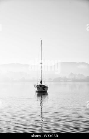 Schöne unplugged Landschaft Bild der Segelyacht sitzt immer noch in ruhigen See Wasser im Lake District während der friedlichen nebligen Herbst Sonnenaufgang Stockfoto