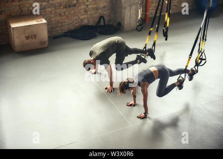 Jung und sportlich. Blick von oben auf ein Paar in Sportbekleidung fitness training mit Trx Träger im Fitnessstudio. Personal Trainer. TRX Training. Zusammen trainieren Stockfoto