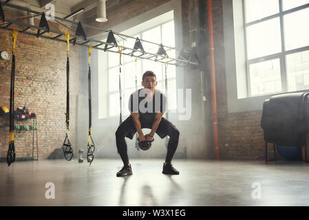 Gewicht ausüben. Stattlich und starken jungen Mann im Sport Bekleidung Training mit Hanteln und Fitnessraum stehen. Bodybuilding Konzept. Training. Gesunder Lebensstil Stockfoto