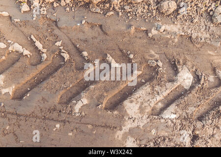 Die Textur der braunen Masse der Sandweg mit Spuren der Reifen von PKW-Reifen des Traktors. Stockfoto