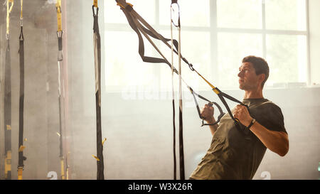 Ich möchte perfekten Körper zu haben. Starke athletischen Mann Training seine Arme mit trx fitness Träger im Fitnessstudio. TRX Training. Training Konzept. Stockfoto