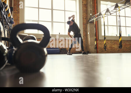 Aufwärmen vor dem Training. Junge sportliche Mann in Sportkleidung zu tun Stretching Übungen im Stehen vor dem Fenster im Fitnessstudio. Training Konzept. Professionellen Sport. TRX Training. Stockfoto