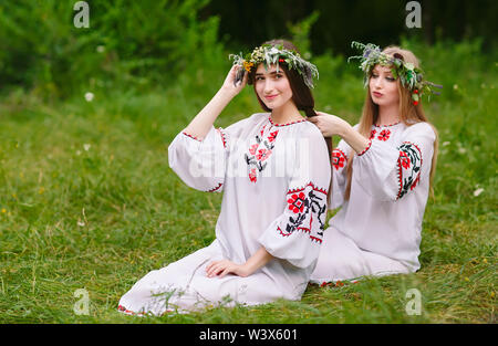 Hochsommer. Zwei Mädchen in der Slawischen Kleider weben Flechten der Haare in der Nähe des FIRE Stockfoto