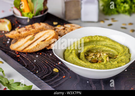 Hummus mit Spinat und Kürbiskerne in einer Schüssel auf einem Holzbrett, orientalische Küche, horizontale Foto Stockfoto