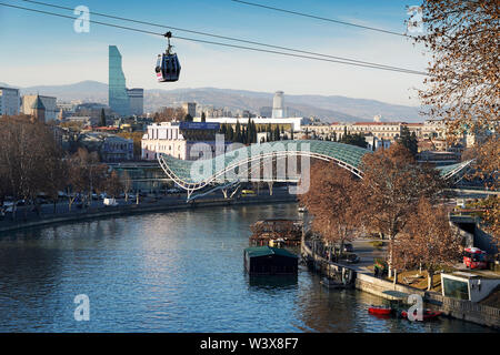 Eine Seilbahn Gondel schwebt über dem Mtkvari River. Im Hintergrund: die Brücke des Friedens von Michele De Lucchi. Der Innenstadt von Tiflis, Georgien, Kaukasus Stockfoto