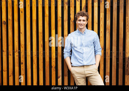 Junger Mann mit Smart casual Outfit, gegen einen hölzernen Wand auf der Straße von einer europäischen Stadt Stockfoto