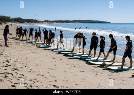 Eine Gruppe junger Rucksacktouristen, die ihren ersten Surfunterricht mit einem Lehrer an der Agnes Water Beach Caravan und dem Campingplatz in Queensland, Australien, haben. Stockfoto