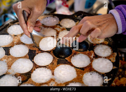 Mörtel - geröstete Gebäck oder "Kanom Krok' ist für traditionelle thailändische Dessert. Frau Hand entfernen Kanom Krok von Herd durch die Löffel. Street Food in Thailand. Thai Stockfoto