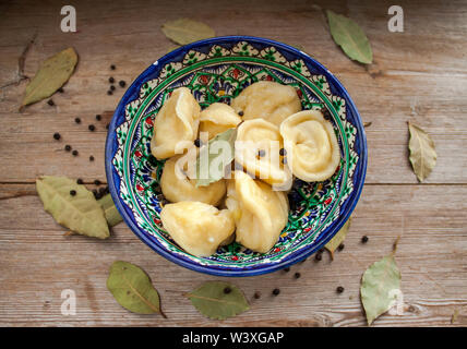 Knödel mit Kartoffeln gefüllt oder Treffen und serviert mit Butter oder Rahm in Blau und Grün orientalische Teller auf rustikalen Holzmöbeln Hintergrund der Ansicht von oben. Stockfoto