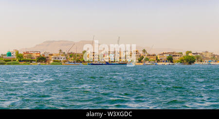Luxor, Ägypten - 16. April 2019: Wohngebäude auf dem Nil mit Segelbooten in Luxor, Ägypten Stockfoto