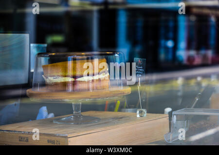 Ein Blick durch ein Coffee shop Fenster von handgefertigten Victoria Schwamm Kuchen zum Verkauf mit Spiegelungen im Glas Stockfoto