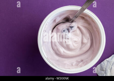 Joghurt becher mit Blue Berry Joghurt, Löffel und Folien Deckel auf lila Hintergrund mit Text Raum isoliert - Ansicht von oben Foto von cremige Frucht Joghurt Stockfoto