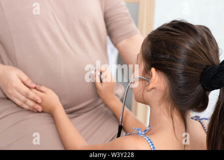 Süße Tochter hört der Baby im Bauch der Mutter zu überprüfen. Schwangere und Eltern. Gesundheit und medizinische Versorgung. Menschen Lebensstile und Familie Konzept. Stockfoto