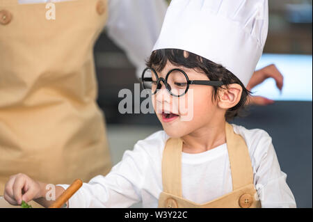 Nahaufnahme des Asiatischen niedlichen kleinen jungen Koch trug Hut und Schürze mit Mutter in der Küche zu Hause. Der Thai und Lebensstile Konzept. Job Beruf und Educat Stockfoto