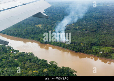Luftaufnahme von innen ein Passagierflugzeug über dem Fluss und Rauch von einem Feuer Clearing für Brandrodung Landwirtschaft in Amazonien von Peru, Südafrika Stockfoto