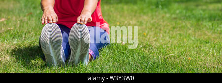 Frau tun, Dehnübungen, sitzend auf natürlichen, grünen Gras im Freien im Garten, Outdoor Training Konzept für Web Banner, Webseite etc. W Stockfoto
