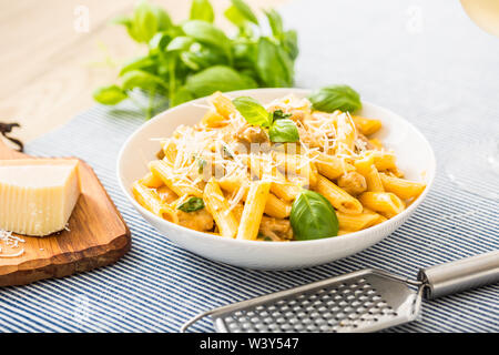 Pasta Penne mit Huhn Stücke Pilze Basilikum Parmesan und weißen Wein. Italienisches Essen in weißen Platte auf dem Küchentisch. Stockfoto