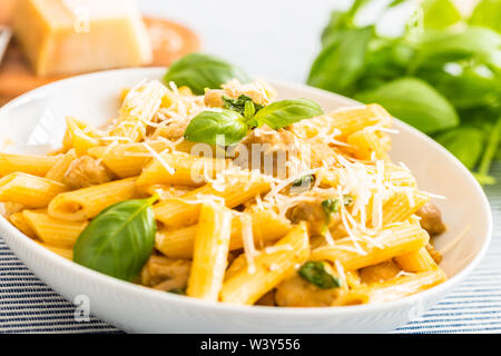 Pasta Penne mit Huhn Stücke Pilze Basilikum Parmesan und weißen Wein. Italienisches Essen in weißen Platte auf dem Küchentisch. Stockfoto