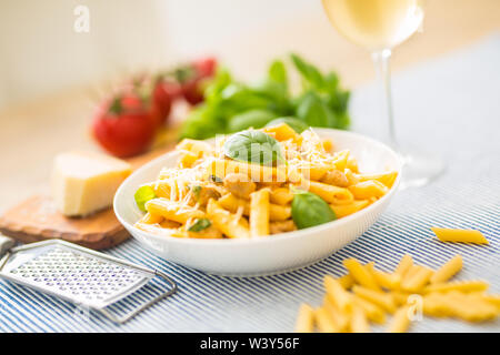 Pasta Penne mit Huhn Stücke Pilze Basilikum Parmesan und weißen Wein. Italienisches Essen in weißen Platte auf dem Küchentisch. Stockfoto