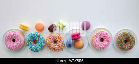 Donuts und Französische macarons auf weißem Tabelle, Ansicht von oben, Banner, kopieren Raum Stockfoto