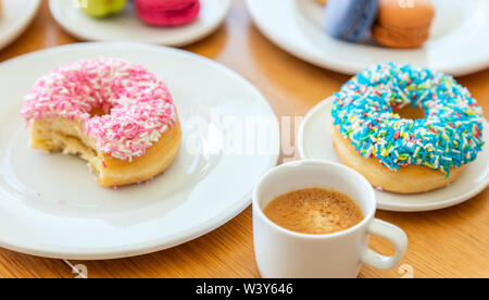 Donuts und französische Macarons, esresso Kaffee auf Holztisch, Ansicht schließen mit Details. Stockfoto