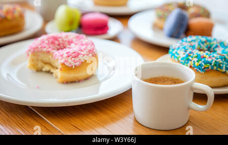 Donuts und französische Macarons, esresso Kaffee auf Holztisch, Ansicht schließen mit Details. Stockfoto