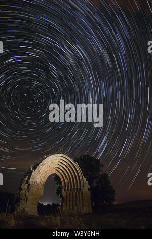 Nacht Bild eines Zirkumpolar mit den Ruinen von St. Michael arch im Sasamon, Burgos (Spanien) im Vordergrund. Stockfoto