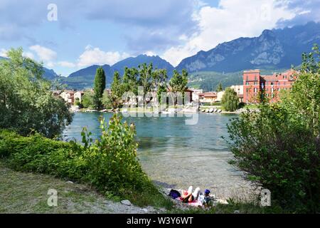 Lecco/Italien - Juli 10, 2014: Paar touristische Relaxen am Ufer des Adda in Lecco Pescarenico fisherman Bezirk, mit Bergen über. Stockfoto