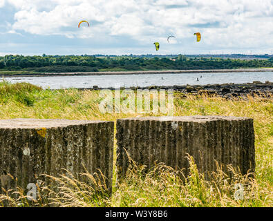 Longniddry Bents, East Lothian, Schottland, Vereinigtes Königreich, 18. Juli 2019. UK Wetter: Sehr windig sonniger Tag ist ideal für Kiter, die in Kraft sind, da die Flut in den Firth von weiter kommt. Überreste des Zweiten Weltkriegs konkrete Anti-tank Bausteine im Vordergrund Stockfoto