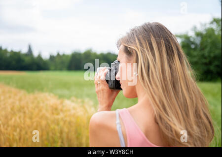 Ansicht von hinten über die Schulter einer jungen Fotografin, die ein Foto mit schwarzen DSLR-Kamera der Felder in der Natur. Stockfoto