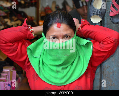 Nepali Hindu saleslady mit einem roten sindoor und Bindi auf ihrer Stirn schützt Ihren Mund und Nase von Luftverschmutzung und Staub mit einem grünen Gesicht bandana. Stockfoto