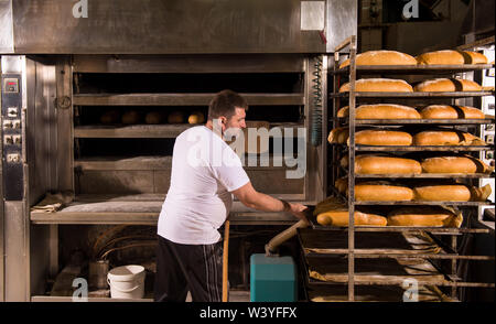Bäckerei Arbeiter aus frisch gebackenes Brot mit Schaufel, die aus dem professionellen Ofen bei der Herstellung Stockfoto