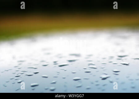 Hintergrund mit unscharfen Tropfen auf das Dach eines Silber blaues Auto und einen grünen Hintergrund. Leichte Steigung über dem Dach. Es ist ein Platz für Text. Stockfoto