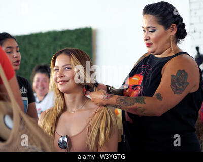 Lächelnde junge blonde Frau, die ihr Haar geflochten durch eine ausgereifte Hispanic Frau an einem 'Loca für Lokale' Event in Corpus Christi, Texas USA. Stockfoto