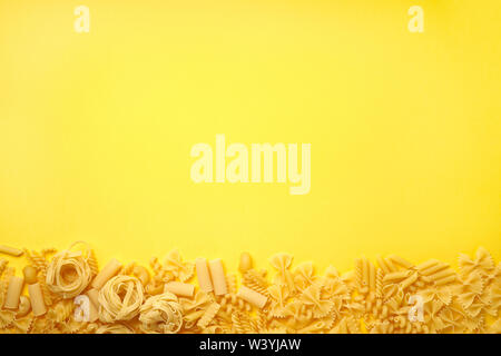 Verschiedene Arten von Pasta auf gelben Hintergrund. Ansicht von oben. Verschiedene Formen der Pasta. Stockfoto