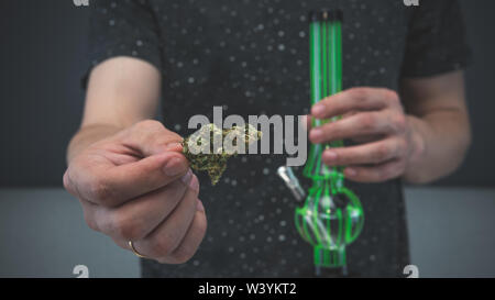 Der junge Mensch in seiner Hand medizinisches Marihuana Knospen und Bong. Die medizinische Verwendung von Cannabis rauchen mit Bong. Marihuana ist ein Konzept der Kräutermedizin Stockfoto