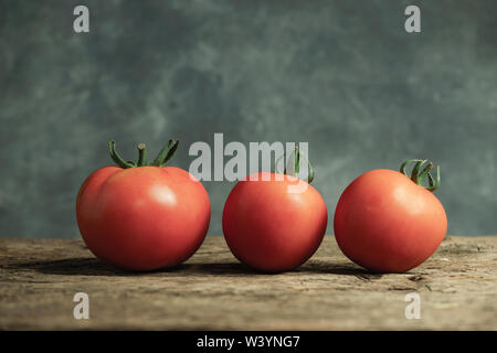 Frische Tomaten auf einer alten Eiche Holztisch, schöne graue Wand Hintergrund. Stockfoto