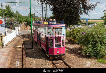 Seaton, Devon, England, UK. Juli 2019. Seaton Tramway. Elektrische Straßenbahn. Straßenbahnwagen und Passagiere vorbei an einem Bahnübergang Stockfoto