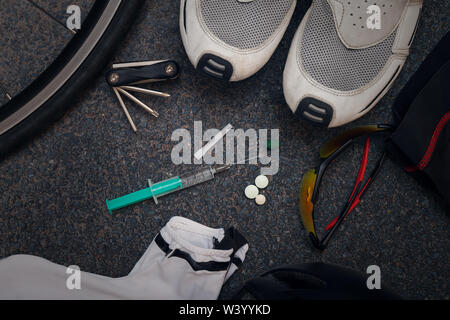 Radfahren Bekleidung und Ausrüstung auf Asphalt mit einer Spritze und Tabletten in der Mitte, zur Veranschaulichung von Doping oder der Missbrauch von Leistungsfördernden Substanzen im Amateur- und im Profisport. Stockfoto