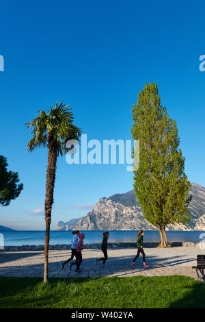 Jogger am North Beach auf Sonnenaufgang am kleinen Hafen Porticcioloat Lago di Garda, Gardasee, Torbole - Nago, Riva, Trentino, Italien am 15. April 2019. Stockfoto