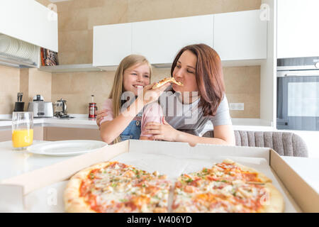 Mutter und Tochter in der Küche sitzen, essen Pizza und Spaß haben. Fokus auf Tochter Stockfoto