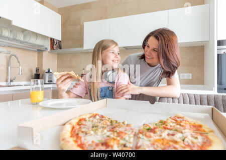 Mutter und Tochter in der Küche sitzen, essen Pizza und Spaß haben. Fokus auf Tochter Stockfoto