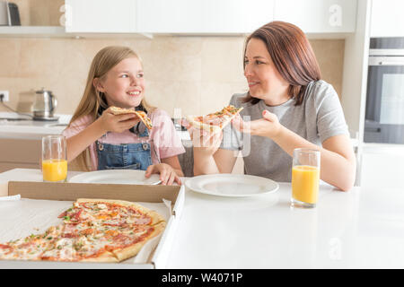 Mutter und Tochter in der Küche sitzen, essen Pizza und Spaß haben. Fokus auf Tochter Stockfoto